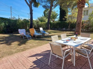 An outdoor patio with a table set for dining, surrounded by lounge chairs and a palm tree. - Magnificent wooded villa, ideally located close to the beach. (L'Escala)