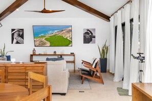 A modern living room with a wooden ceiling, a large flat-screen TV, a dining table, a sofa, a telescope, and a potted plant. - Copala Luxury Villa Oceanview, Private Pool (Cabo San Lucas)