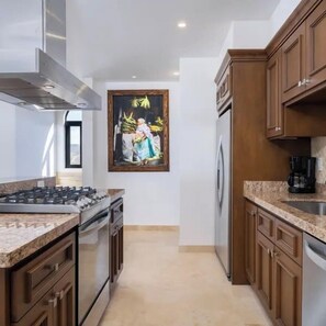 Een keuken met een gasfornuis, oven en vaatwasser, houten kastjes en een schilderij aan de muur.