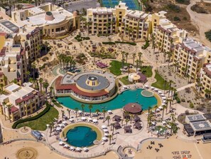 A resort with multiple swimming pools, sun loungers, and a central circular pool area.