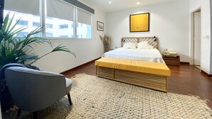 A modern bedroom with a large bed, a chair, a window, and a painting on the wall.