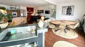 A modern living room with a dining area, kitchen, and a glass wall.