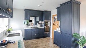 A modern kitchen with dark cabinetry, a wooden countertop, and a built-in oven. - Watlands (Pwllheli)