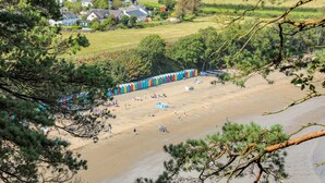 A beach with a row of colorful beach huts, a sandy beach, and houses in the background. - Watlands (Pwllheli)