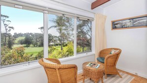 A room with large windows, wicker furniture, a framed picture, and a striped rug. - Tee to Sea - 3BR home with golf & ocean views (Mollymook)