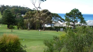 A golf course with a flag, trees, and a house near the water. - Tee to Sea - 3BR home with golf & ocean views (Mollymook)