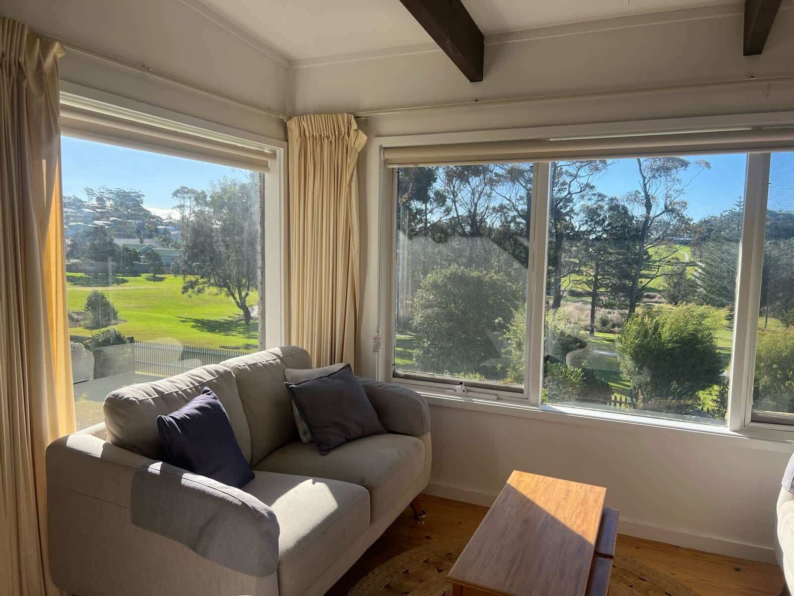 A room with a sofa and a small wooden table, large windows with a view of a green landscape.