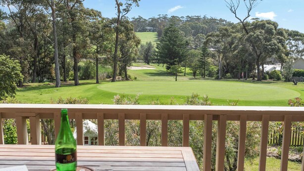 A wooden deck with a bottle and glass, overlooking a golf course with trees and a distant building. - Tee to Sea - 3BR home with golf & ocean views (Mollymook)