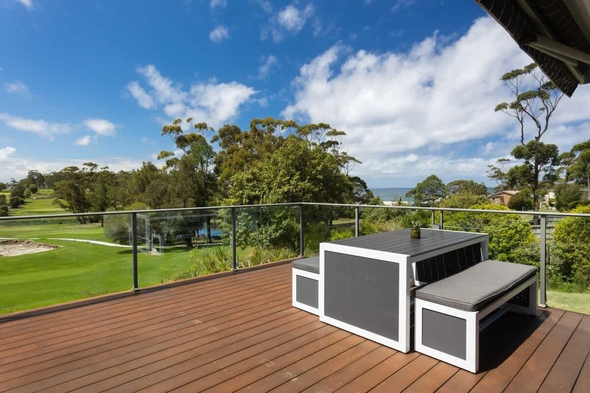 A deck with a table and bench, overlooking a golf course and trees.
