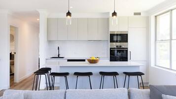 Une cuisine moderne avec des meubles blancs, des appareils électroménagers noirs et un îlot central doté de tabourets.