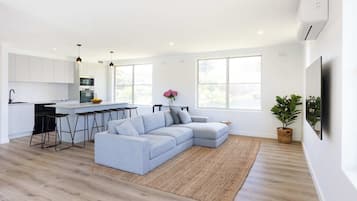 A modern kitchen with white cabinets, a grey sofa, and a dining area with bar stools.