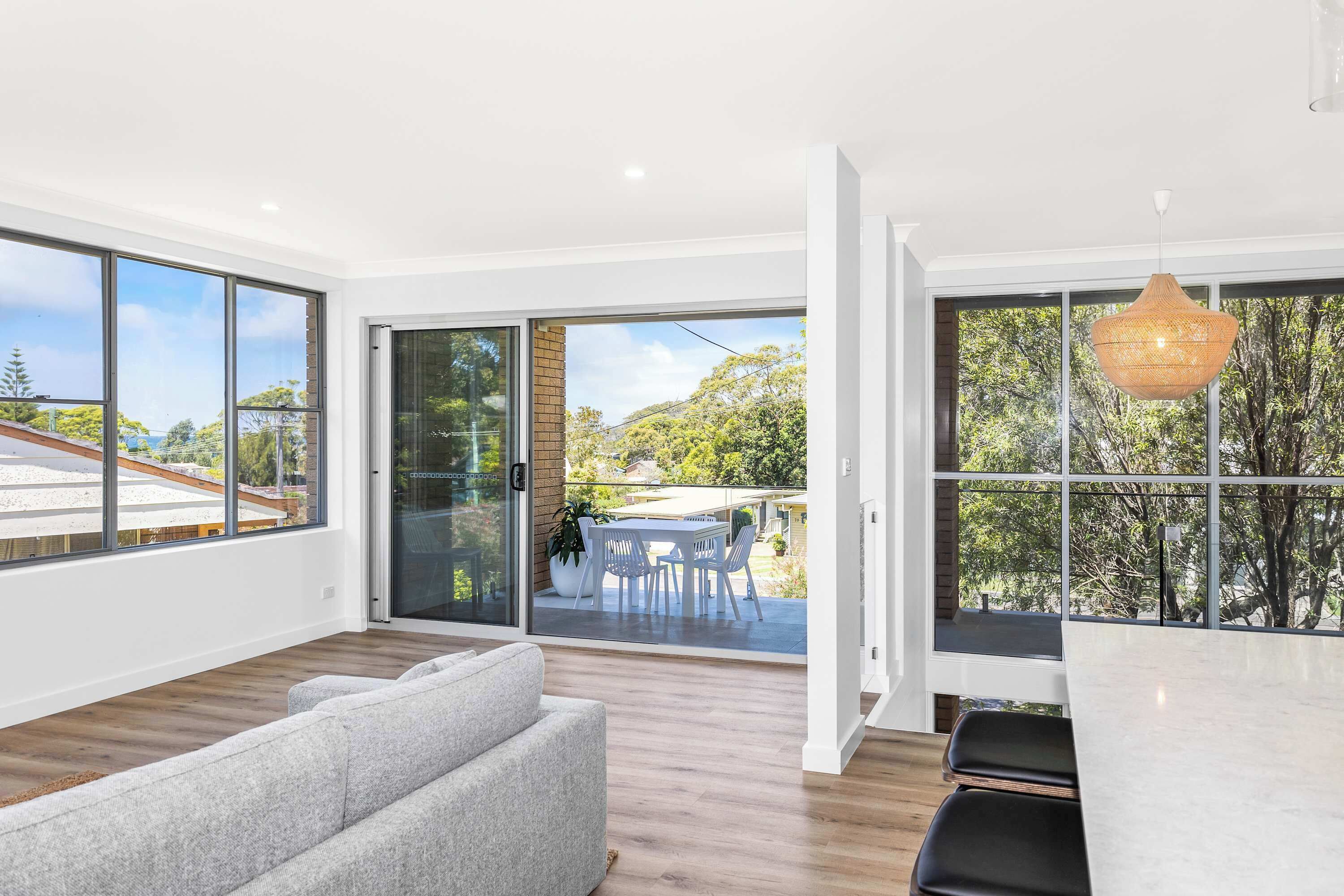 A modern interior with large windows, a dining area with outdoor seating, and a grey sofa.