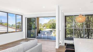 A modern interior with large windows, a dining area with outdoor seating, and a grey sofa.