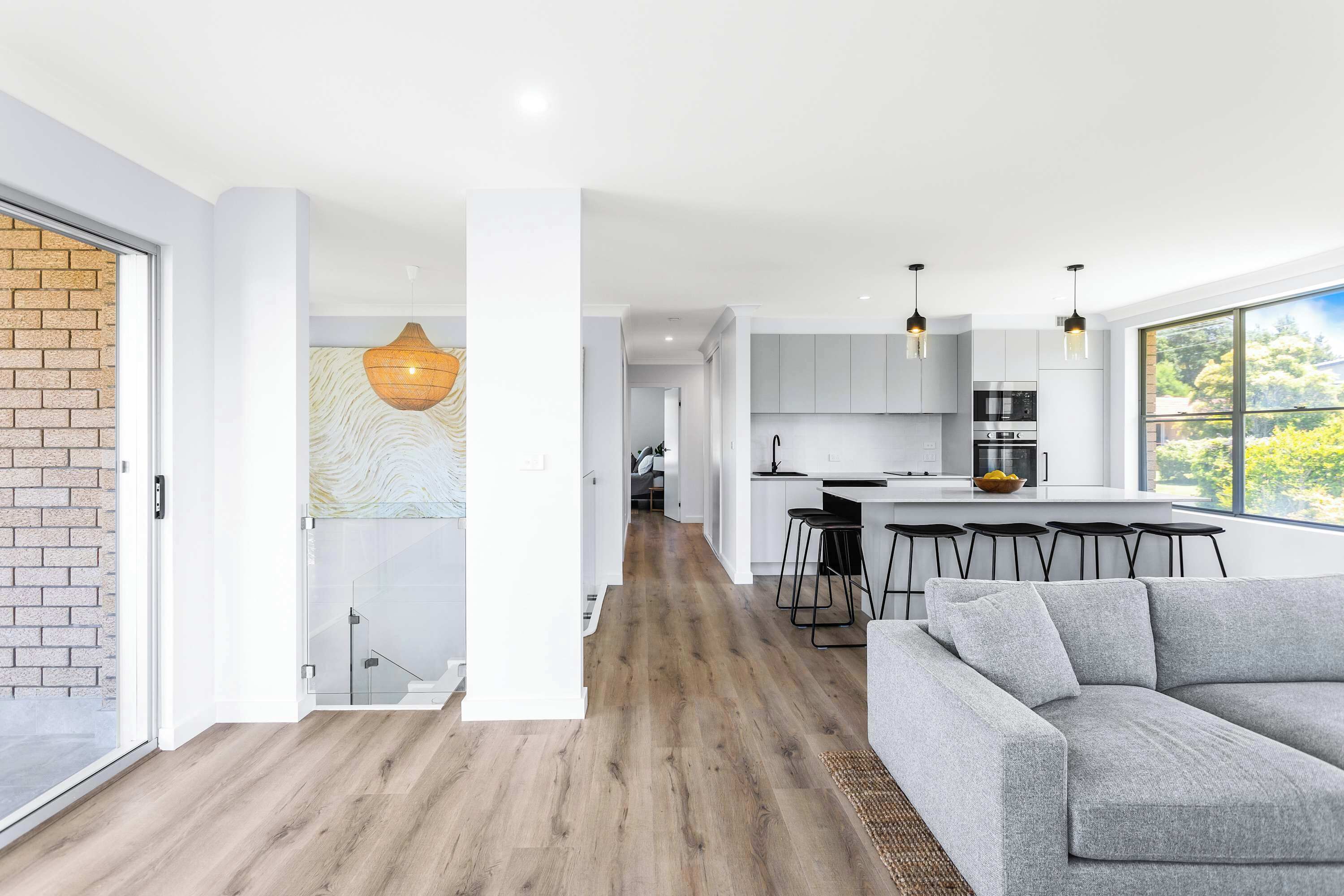 A modern kitchen with a dining area, a grey sofa, and a staircase leading to another level.