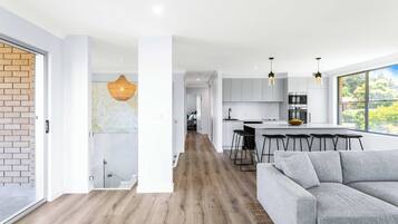 A modern kitchen with a dining area, a grey sofa, and a staircase leading to another level.