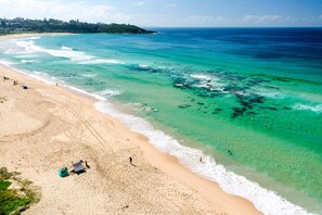 A beach with clear turquoise water, sandy shore, and a few people.