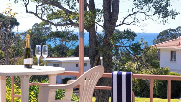 A terrace with a table, chairs, a bottle of wine, and glasses. A striped towel hangs on a railing. - So Close to the Beach (Mollymook)