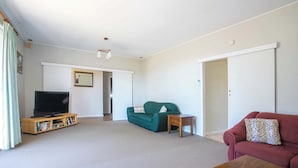 A living room with a television, green sofa, red sofa, wooden coffee table, and a bookshelf. - So Close to the Beach (Mollymook)