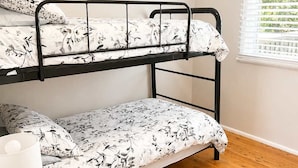 Una cama litera con ropa de cama floral, una mesita de noche con una lámpara y una ventana con persianas.