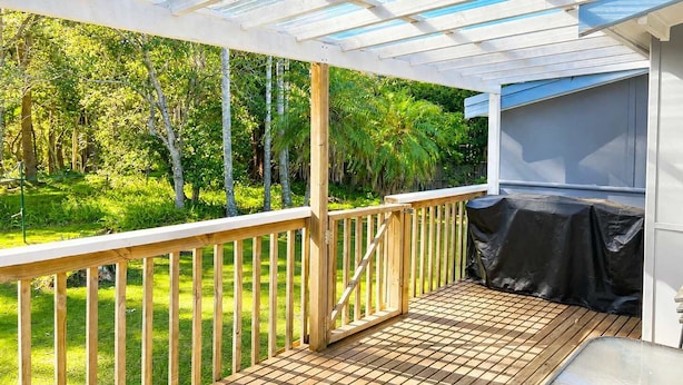 Un espacio al aire libre techado con terraza de madera, una parrilla y vistas a un paisaje verde exuberante.