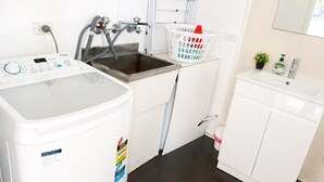 Un área de lavandería con lavadora, lavamanos y un mueble pequeño.