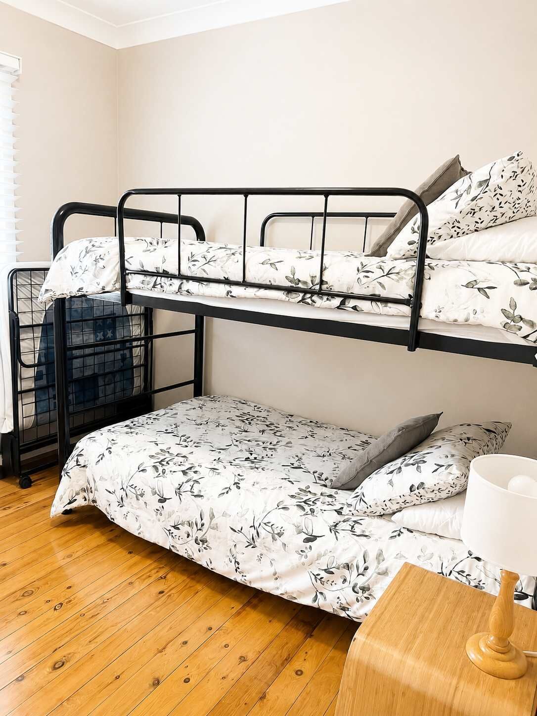 Ein Stockbett mit Blumenmuster, ein Holzboden und ein Nachttisch mit Lampe.