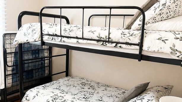 Una cama litera con ropa de cama floral, suelo de madera y una mesita de noche con una lámpara.