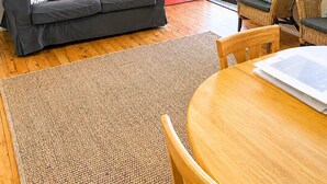 Una sala de estar con un sofá gris, una puerta roja, muebles de mimbre y un cuadro en la pared.