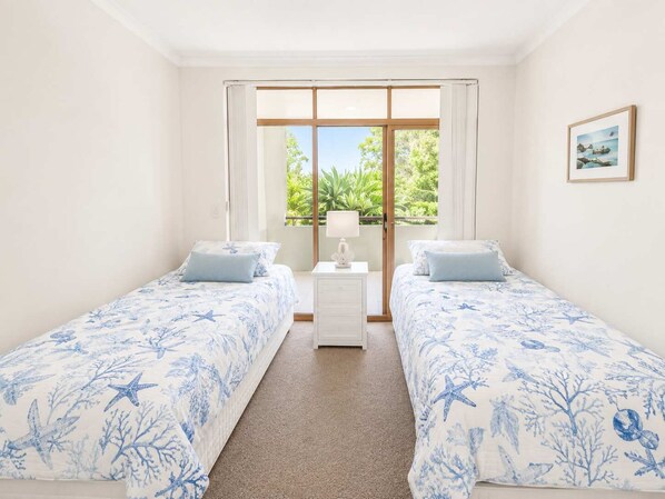 A bedroom with two beds, a nightstand, a window with curtains, and a framed picture on the wall.