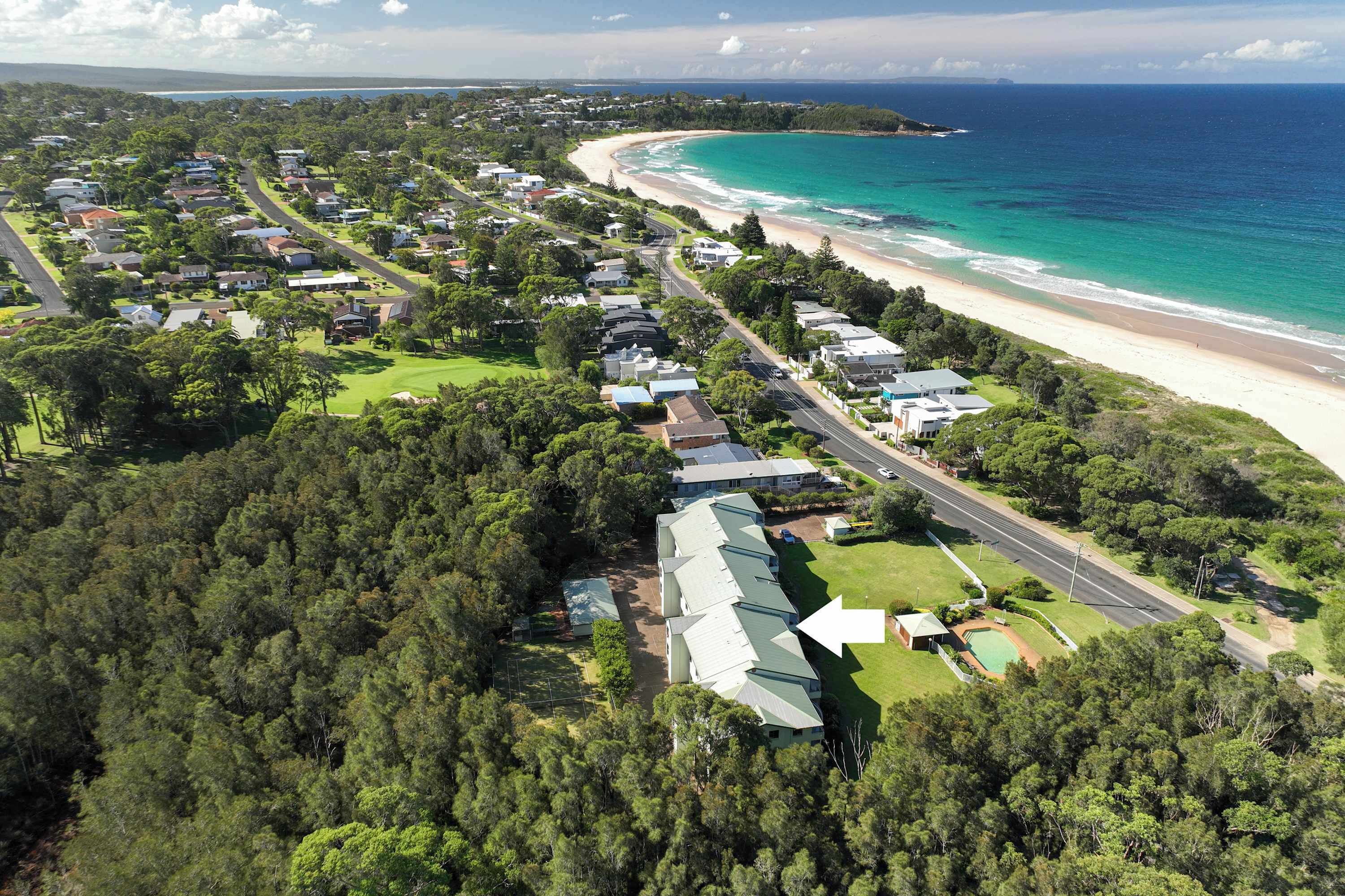 Luchtbeeld van een kustgebied met woningen, een strand en een bebost gebied.
