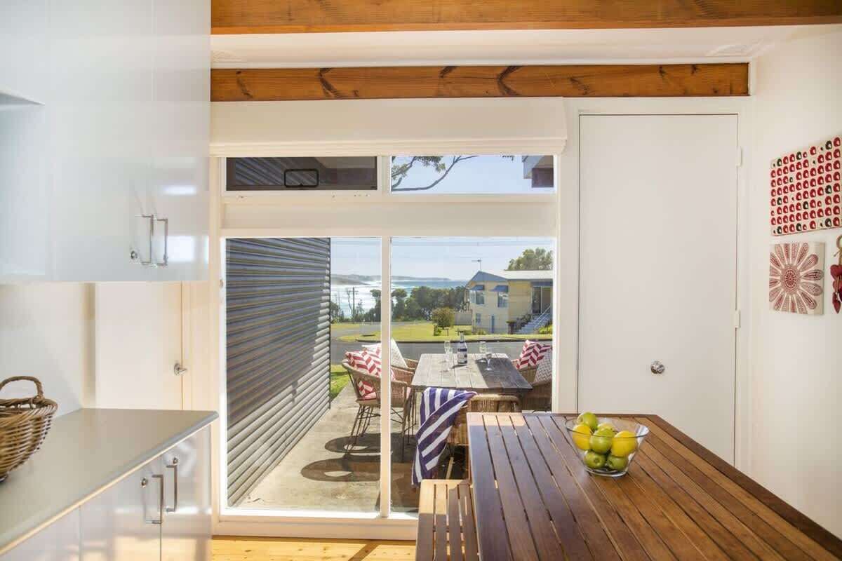 A kitchen with a sliding glass door leading to a patio with a table and chairs, and a bowl of fruit on the table.