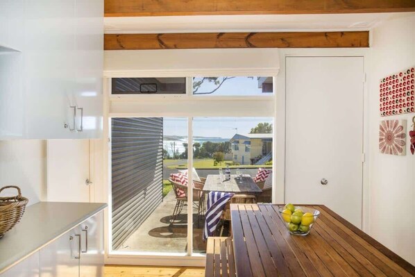 A kitchen with a sliding glass door leading to a patio with a table and chairs, and a bowl of fruit on the table.