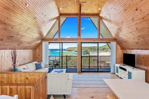 A wooden interior with a large sliding glass door leading to a balcony with a view of the ocean. - Sea-renity Kioloa NSW (Kioloa)