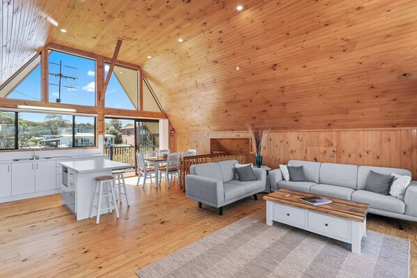 Un ampio loft con soffitto alto, travi in legno, angolo cottura, un divano grigio e un tavolo da pranzo.