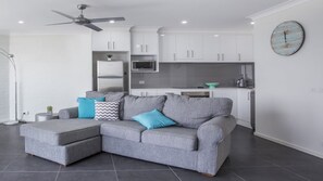 Relax in this stylish living room with a comfortable sofa, kitchenette, and ceiling fan.