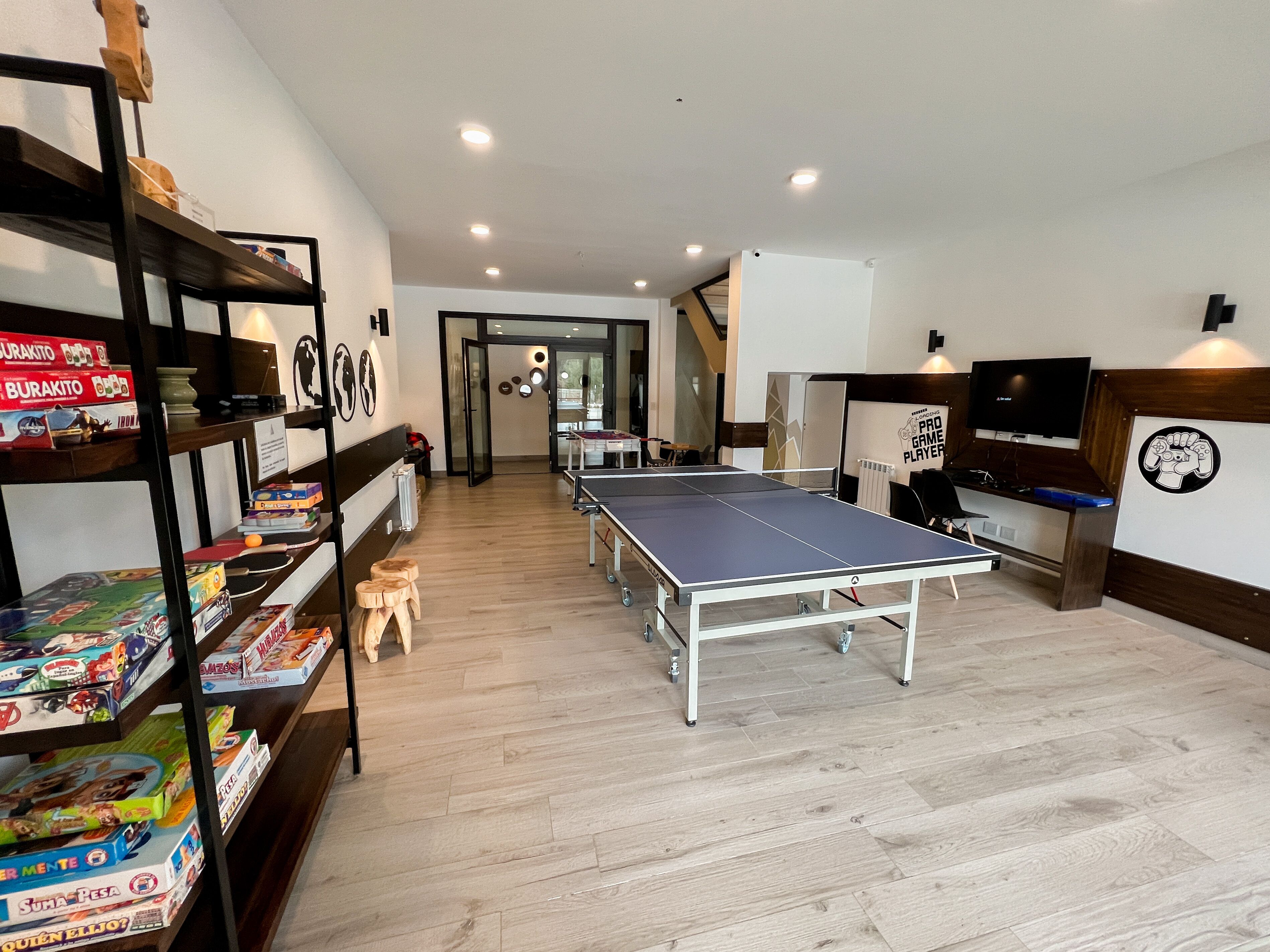 Um quarto espaçoso com mesa de pingue-pongue, prateleiras com jogos de tabuleiro e uma televisão.