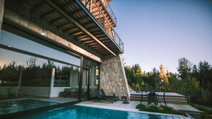 A modern house with a swimming pool, stone exterior, and outdoor seating area. - Awka Apart Hotel (Villa La Angostura)