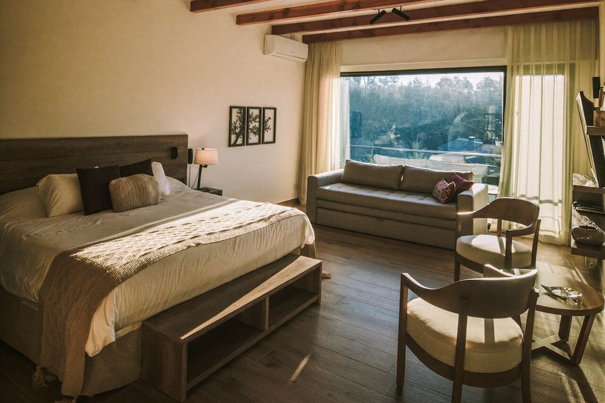 A bedroom with a large bed, a sofa, a chair, and a window with a view.