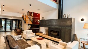 A spacious living area with a fireplace, high ceilings, and a mezzanine level. - Awka Apart Hotel (Villa La Angostura)