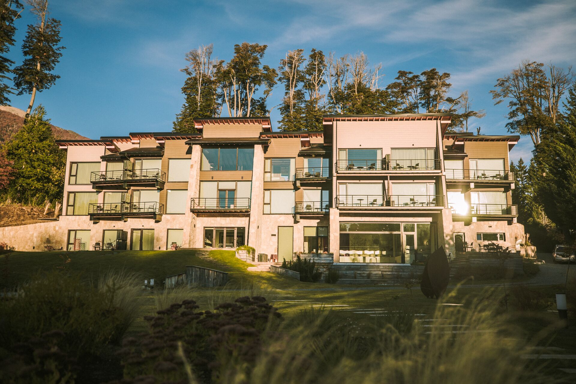 A multi-story building with balconies, large windows, and a well-maintained lawn.