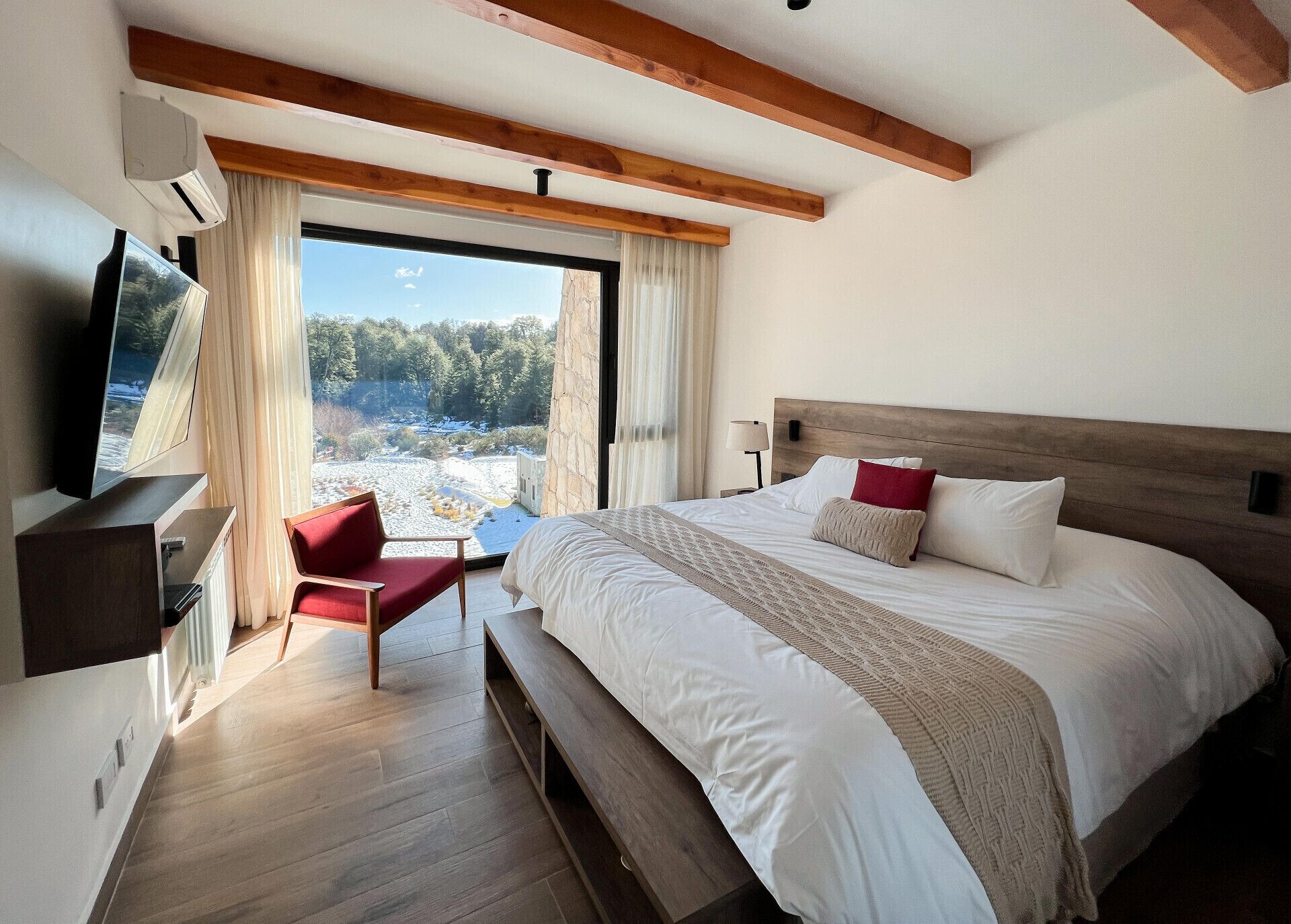 A hotel room with a large bed, a television, a red chair, and a view of a snowy landscape through the window.