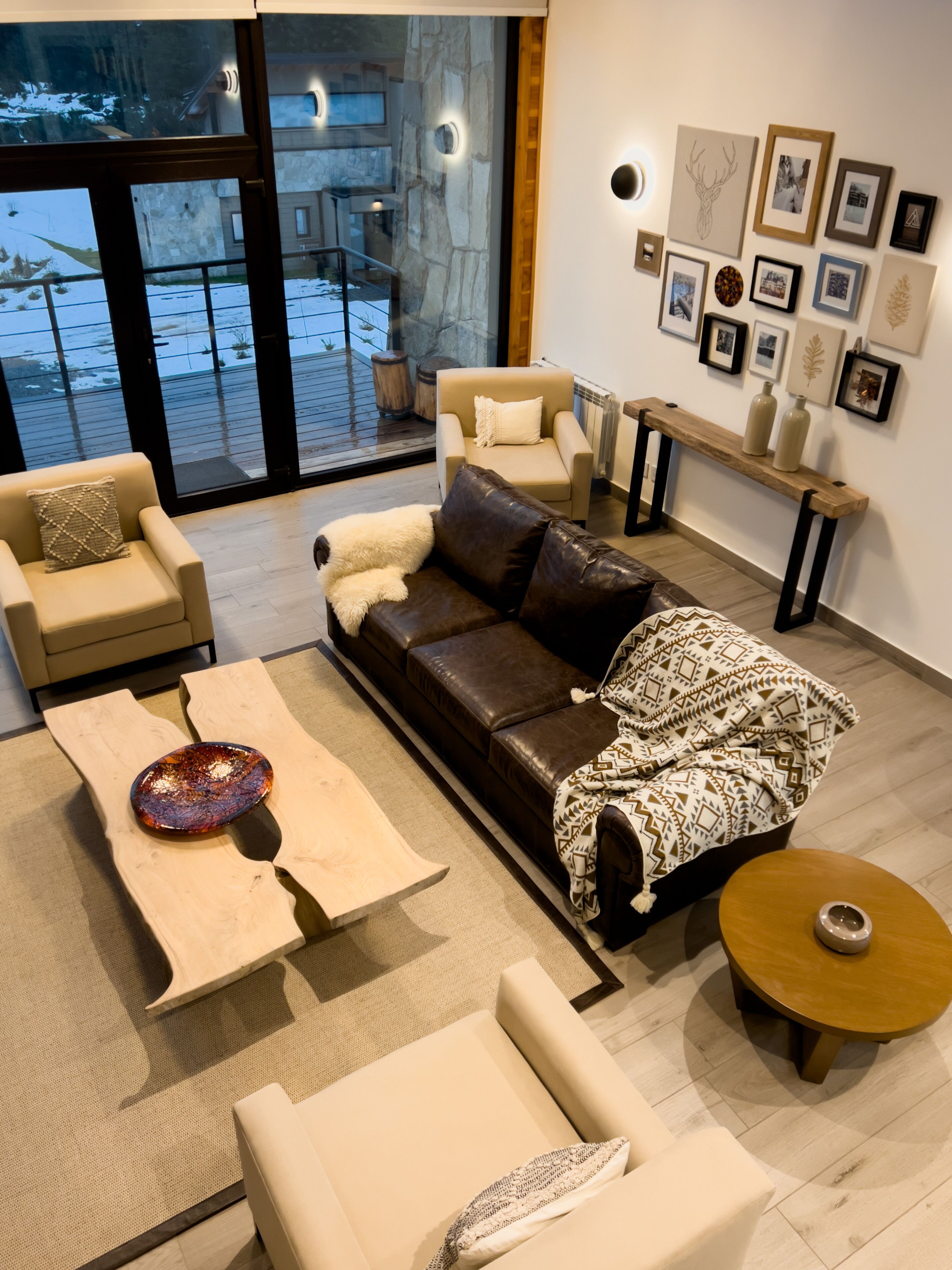 Un salon moderne avec un canapé en cuir, un fauteuil beige et une table basse. Des tableaux encadrés ornent le mur, et un banc en bois est également présent.