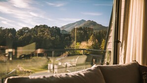 A balcony with a view of a mountainous landscape, a glass railing, and a sofa. - Awka Apart Hotel (Villa La Angostura)