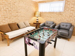 A room with a foosball table, a sofa, and two armchairs. - Magnificent Outlook (Mollymook Beach)