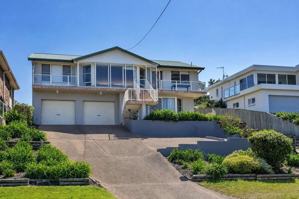 A two-story residential building with a balcony, a garage, and a landscaped driveway.