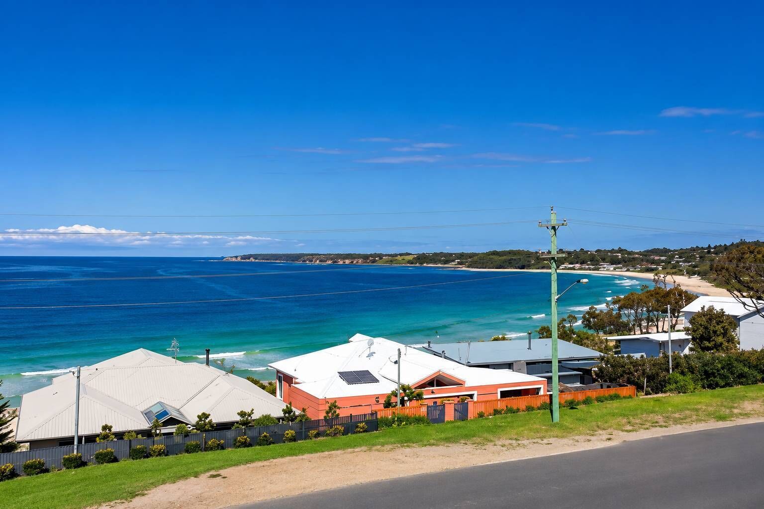 A coastal property with a view of the ocean, a road, and a fenced area with houses.