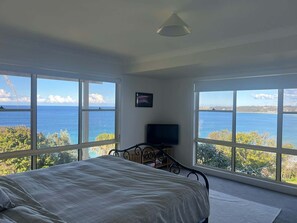A bedroom with a bed, a television, and large windows offering a view of the sea.