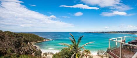 A coastal view with a clear sky, a beach, and a balcony overlooking the ocean.