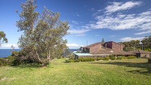 A house with a large lawn, a view of the sea, and a wooden deck. - Stunning Clifftop Location (Mollymook Beach)