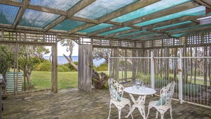 A covered patio area with a table and chairs, a view of the sea, and a wooden fence. - Stunning Clifftop Location (Mollymook Beach)